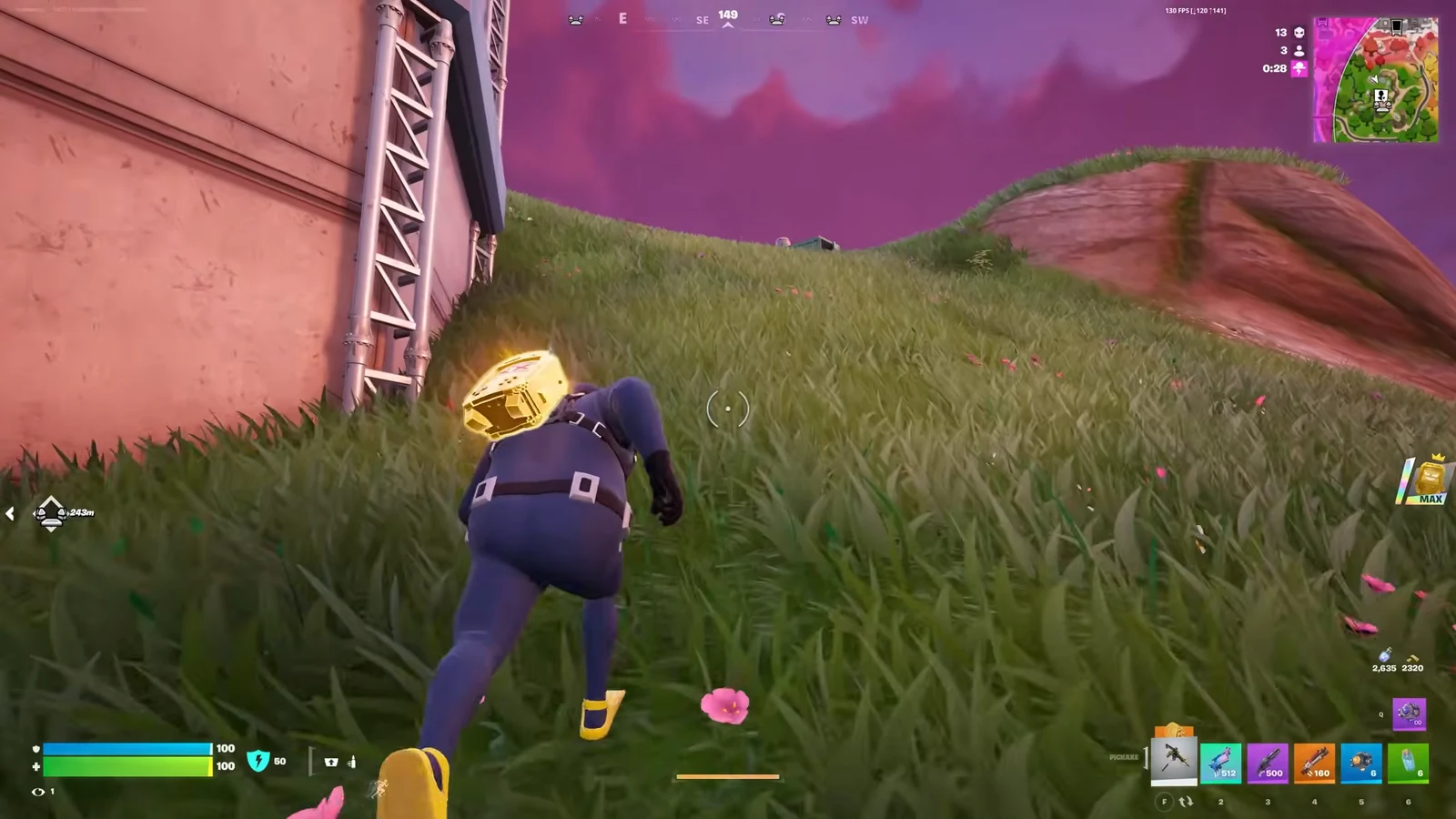 Fortnite player crouch-walking uphill through tall grass beside a building while carrying a glowing gold item