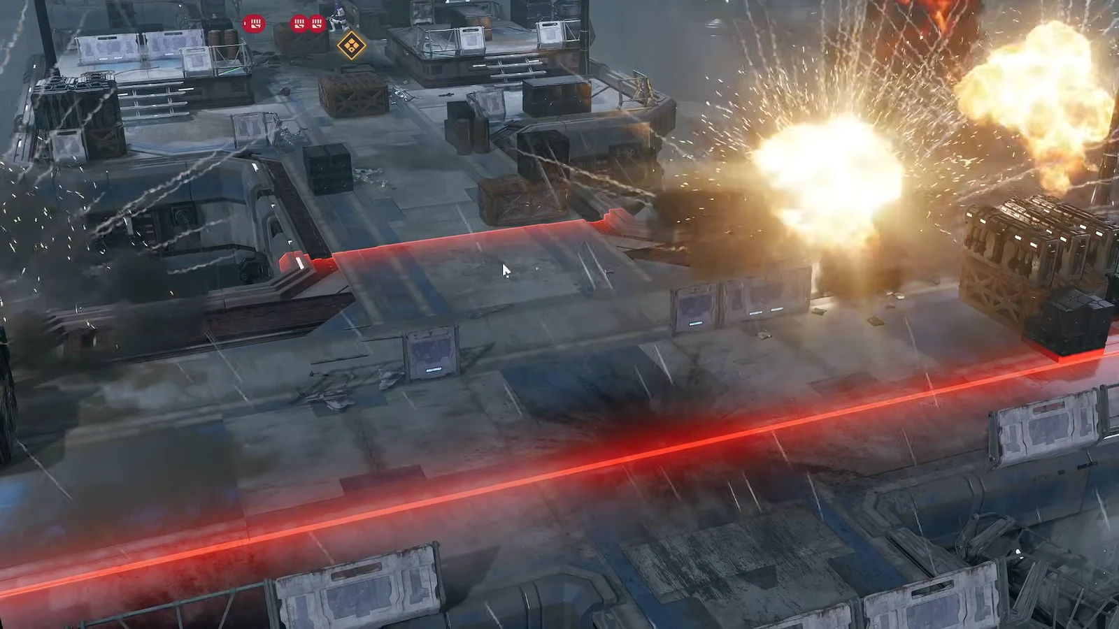A glowing red laser barrier cuts across the arena as explosions go off among crates and platforms