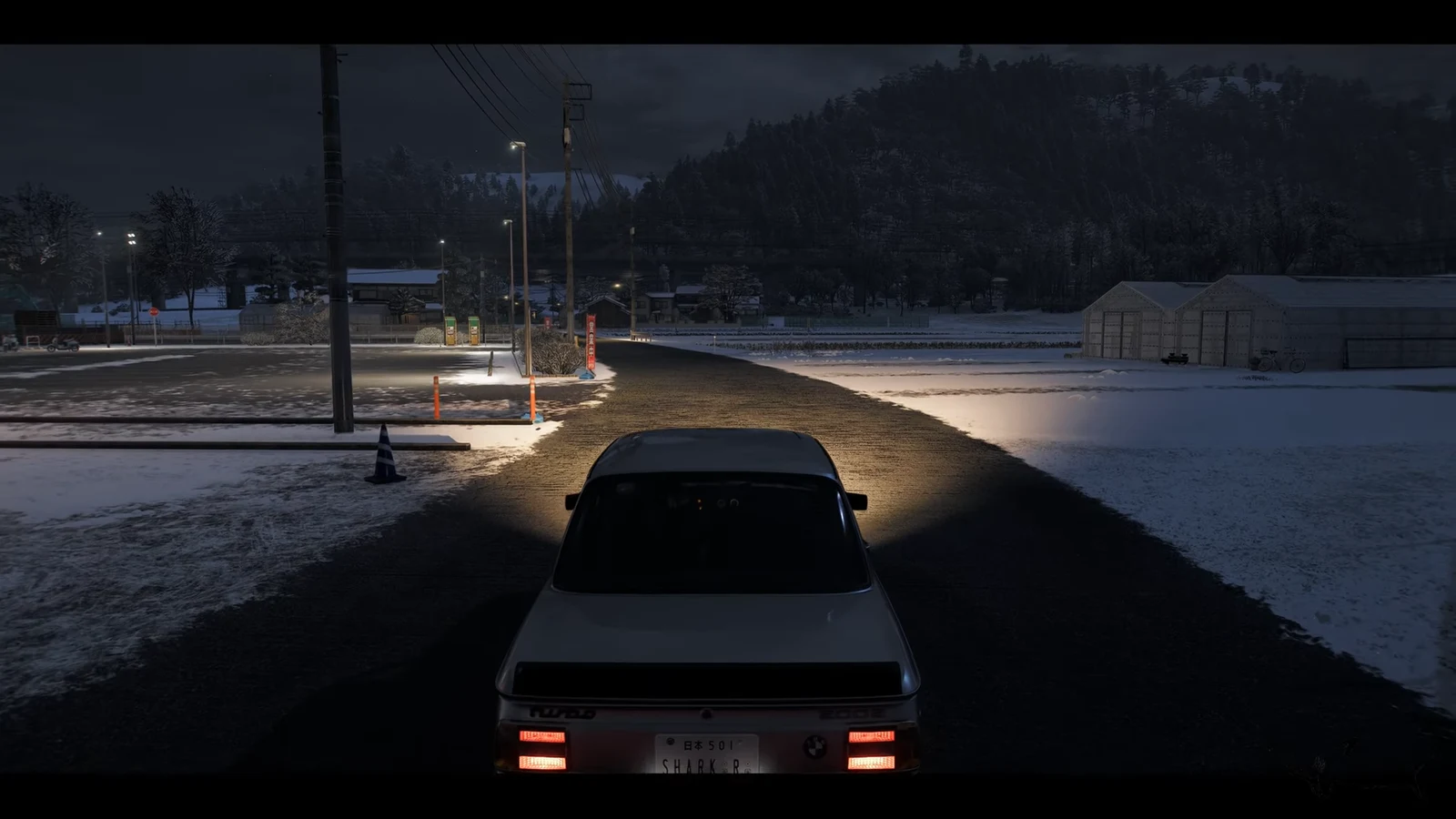 Third-person view of a white car on a snowy road at night beside a rural parking area