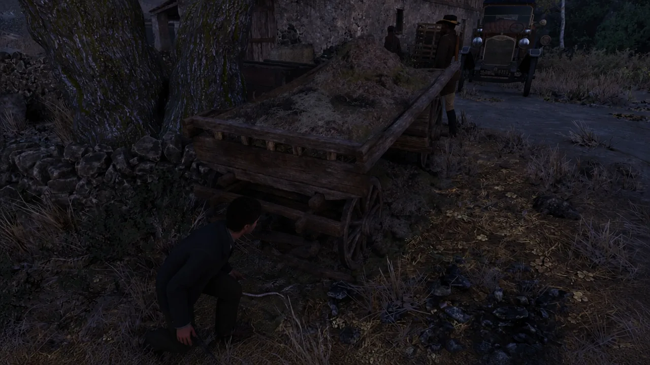 A crouching character takes cover behind a hay-filled wooden cart beside a parked truck