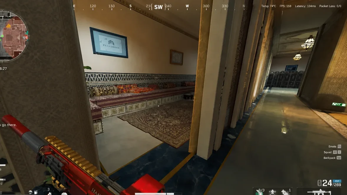 Player peeks through a hotel doorway into a furnished room and corridor while aiming a red rifle