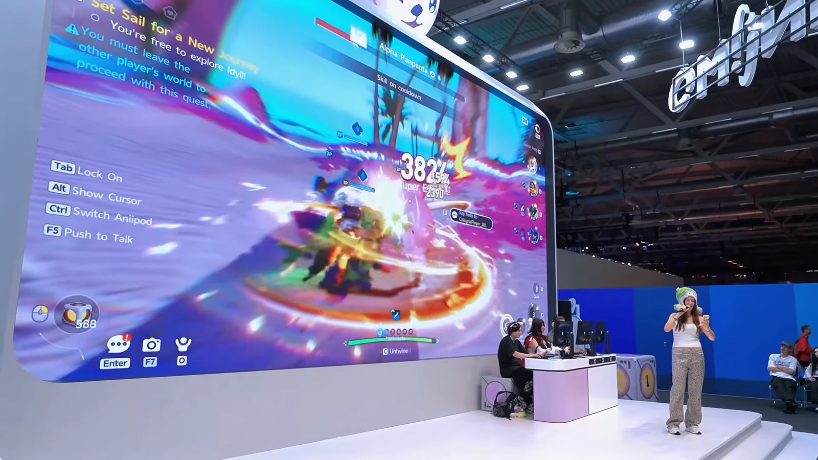 A large exhibition screen shows an Aniimo creature battle with combat effects and gameplay interface beside a presenter on the convention floor.