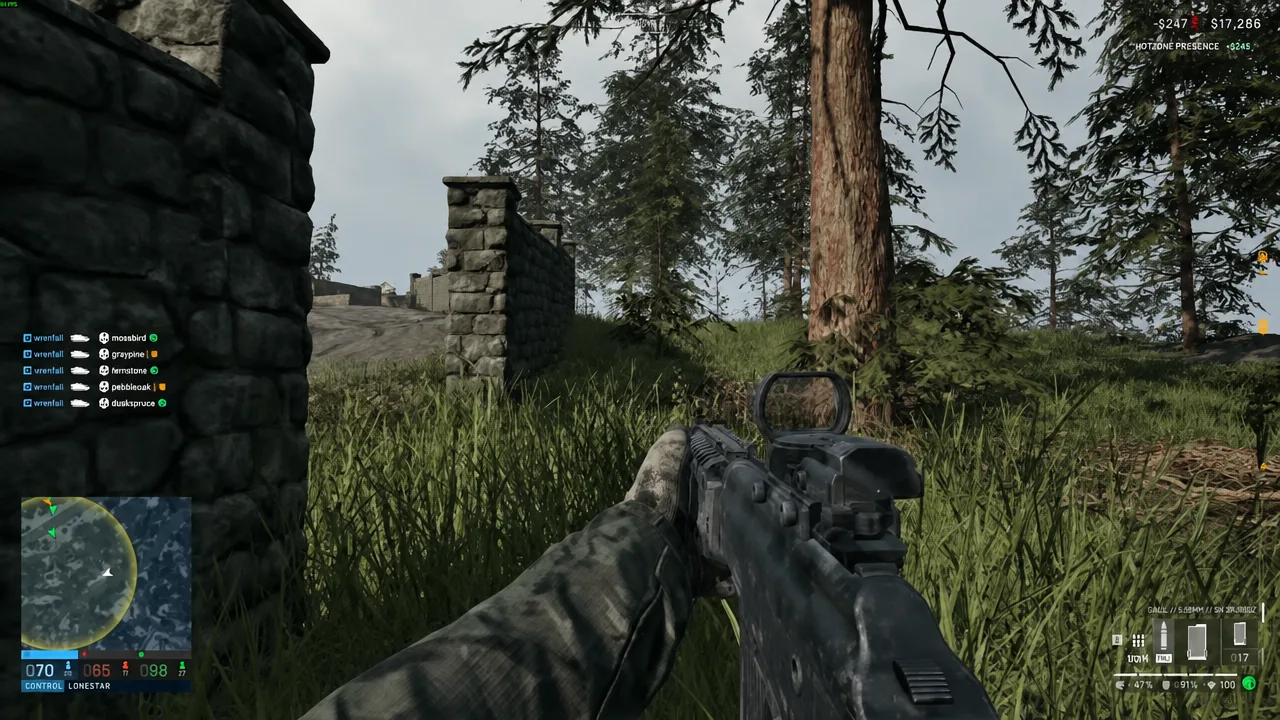 First-person view of a rifle held through tall grass next to a stone wall in a forested area
