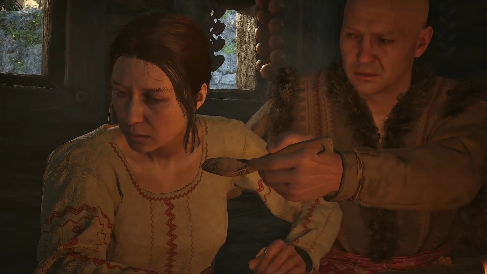 Cutscene of a man feeding an ailing woman with a wooden spoon inside the hut