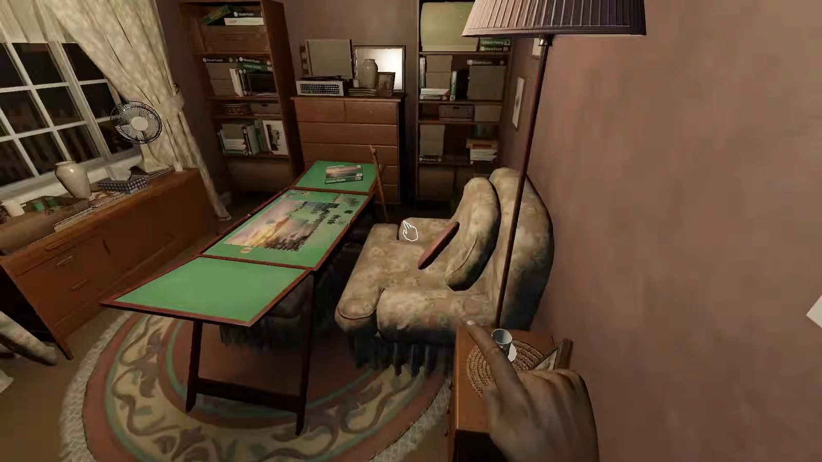 First-person view of an armchair with the hand interaction prompt visible while searching a room
