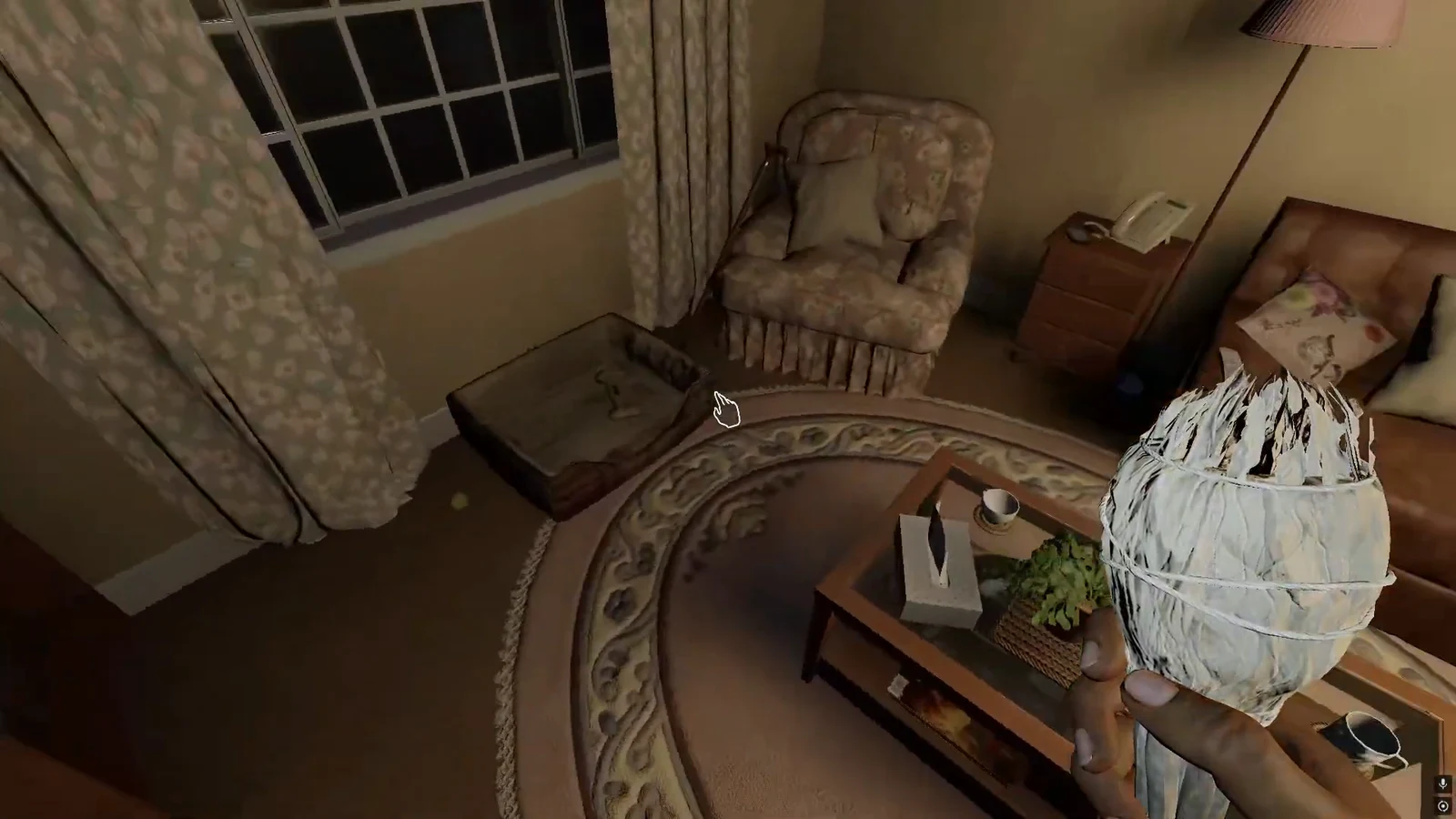 First-person view of a hand cursor over a closed case beside an armchair in a dark living room