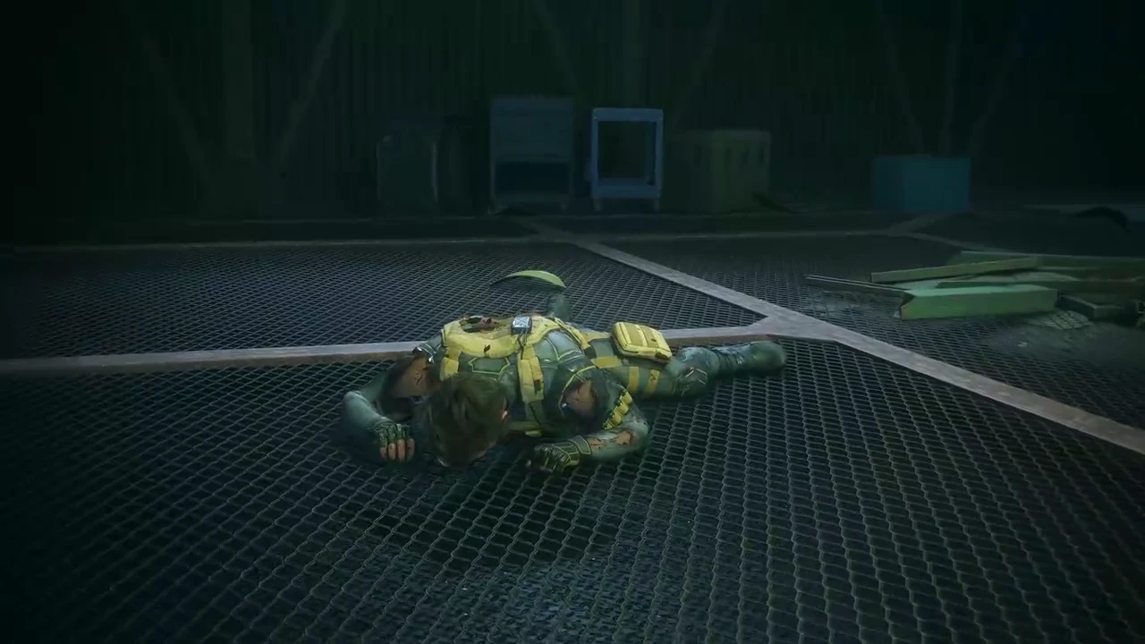 A downed armored figure lying face-first on a metal grate floor inside the dark warehouse arena