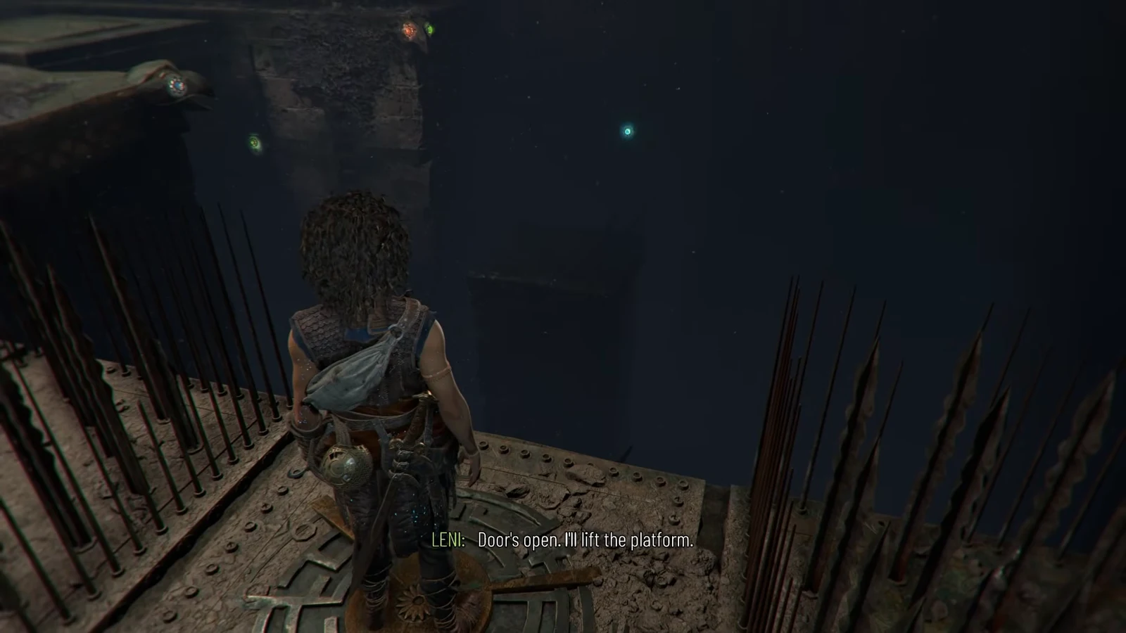 Sophia stands on the raised lift platform beside spikes as Leni calls out that the door is open