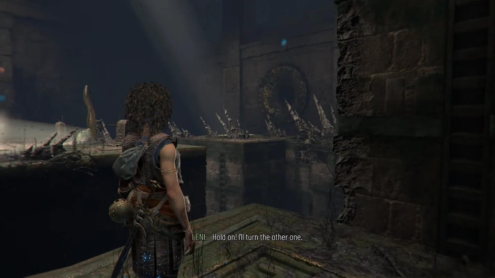 Sophia waits on a ledge facing a spiked platform and a blue-marked wall mechanism as Leni works the far crank