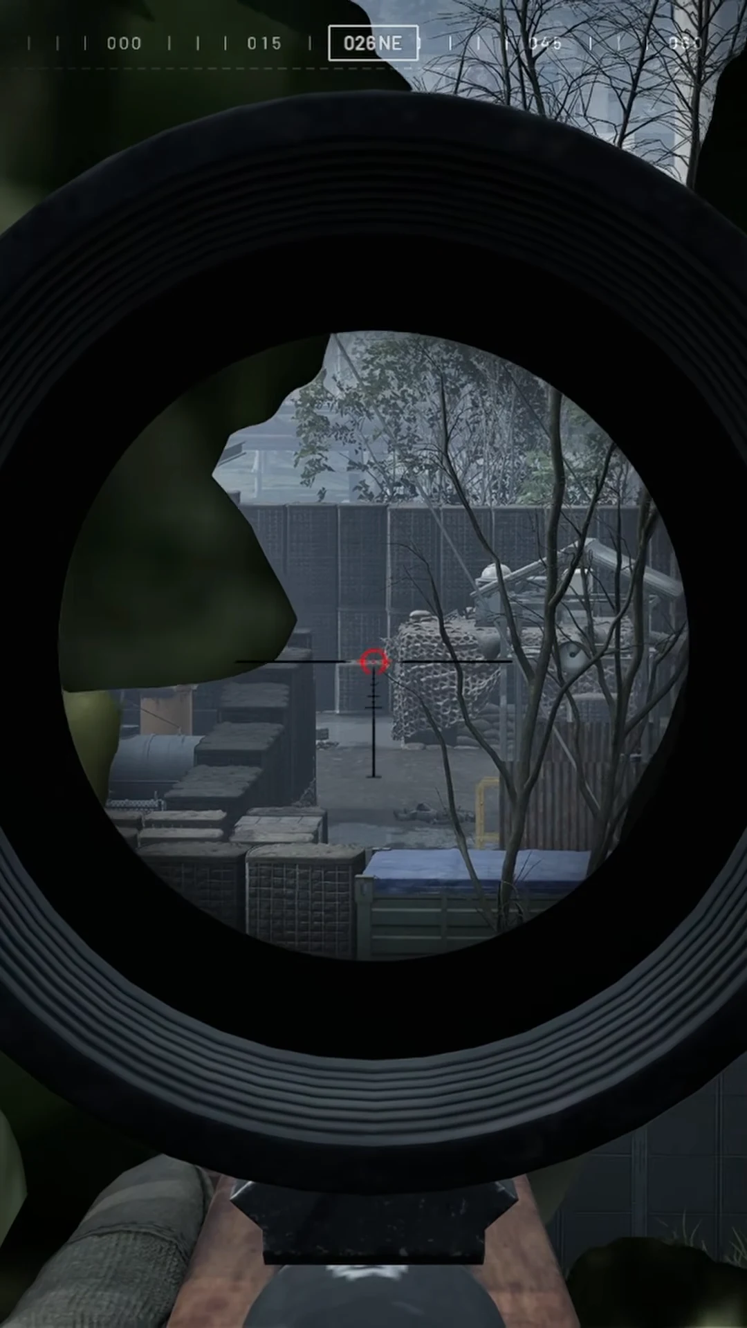 Sniper scope centered on a camouflaged enemy in an industrial yard with the compass reading 026 NE