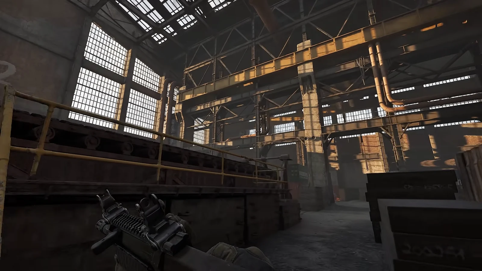 First-person view carrying a rifle through an industrial factory beneath catwalks and piping