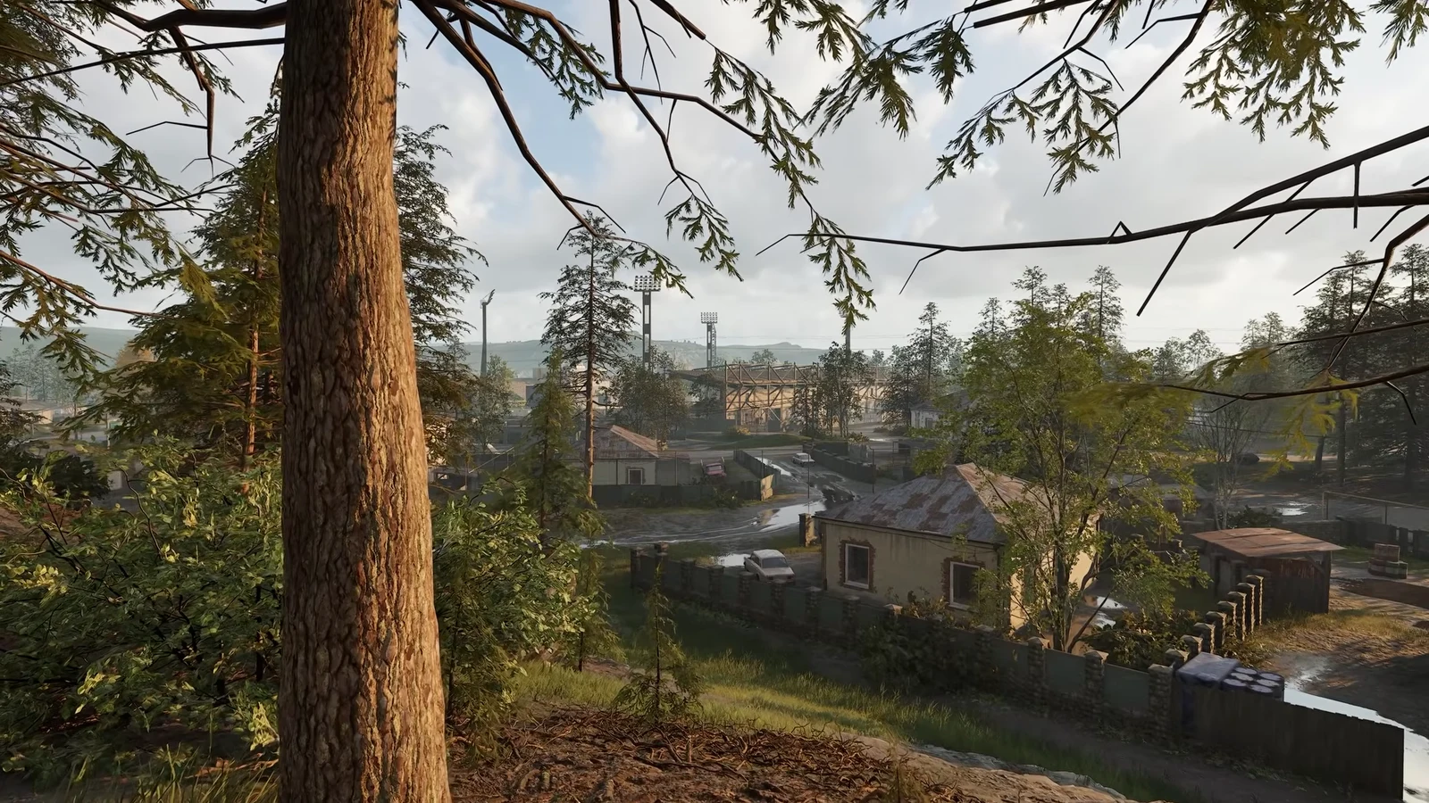 Sunny view of a rural village and distant floodlight towers from a wooded hillside