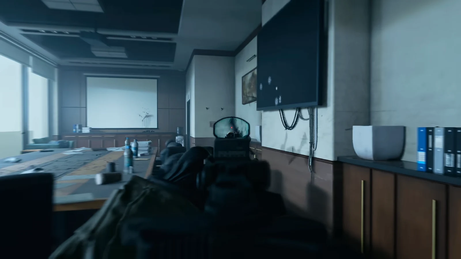 First-person view down a rifle's red-dot sight, aimed across a conference room at the far wall