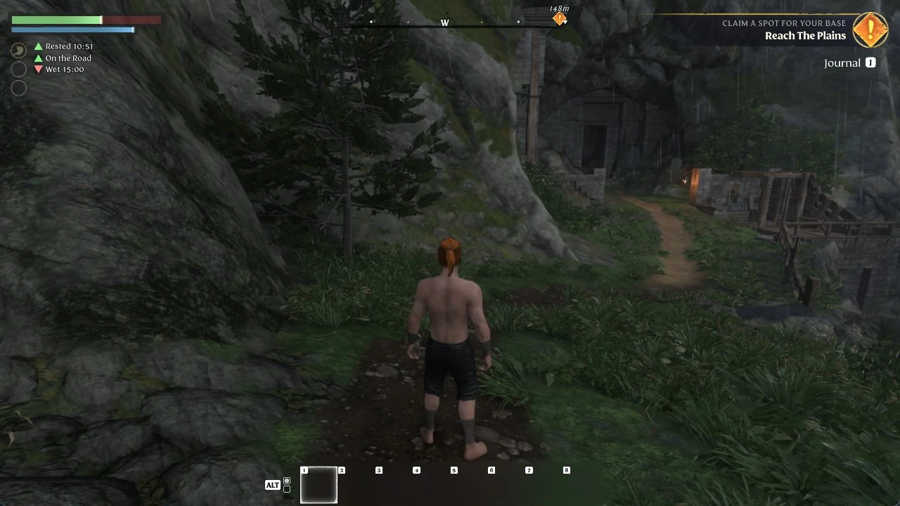 Shirtless character walks a dirt path beside a mossy cliff toward a stone archway and wooden structures in the rain.