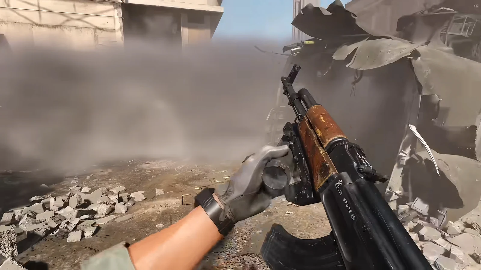 First-person view reloading an AK-style rifle among rubble in a dusty combat zone