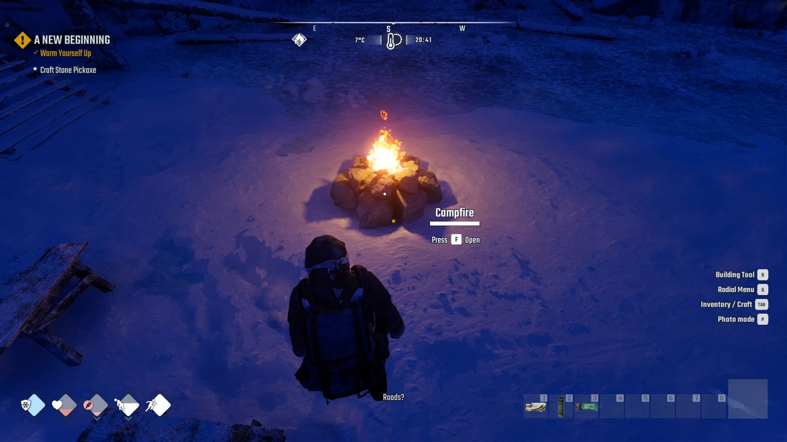A player in a backpack stands in the snow at night facing a burning stone campfire with an Open prompt.