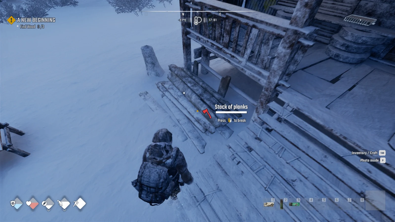 Player in a heavy winter coat crouches in deep snow beside a stack of planks next to a wooden porch, with a break prompt.